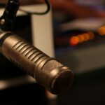 Microphone professionnel dans un studio de radio, entouré d’un éclairage tamisé et d’un arrière-plan flou où l’on devine le matériel de diffusion.