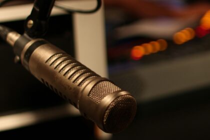 Microphone professionnel dans un studio de radio, entouré d’un éclairage tamisé et d’un arrière-plan flou où l’on devine le matériel de diffusion.