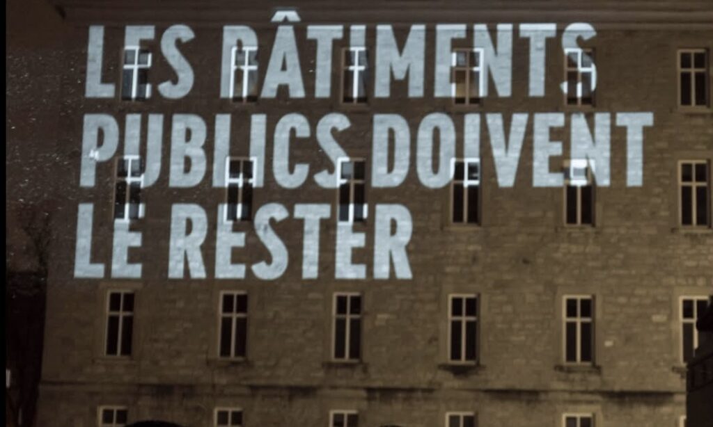 Projeté en blanc sur l’hôtel-dieu de montréal on peut lire « Les bâtiments publics doivent le rester » 