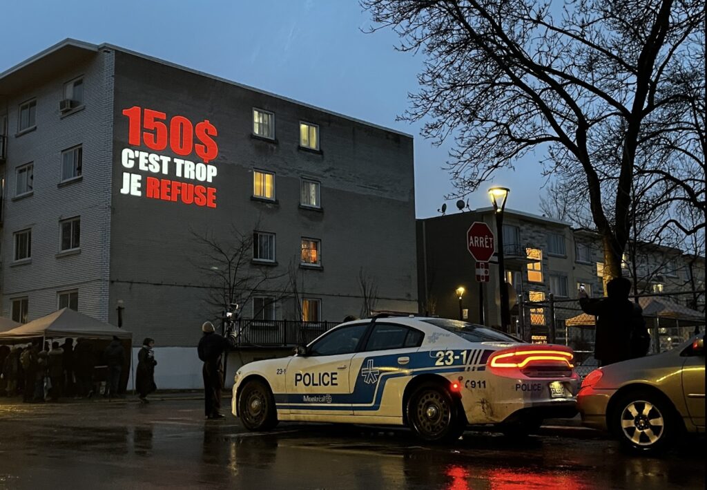 Une voiture de police est stationnée devant un immeuble sur lequel on peut lire en blanc et en rouge « 150$ c’est trop je refuse »