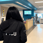 Vue de dos de la Dre Awrad Almesafer, unes des fellows internationaux au Québec, originaire du Koweït, marchant dans le corridor de l'Unité de soins intensifs pédiatriques du Centre universitaire de santé McGill. Elle porte une veste noire sur laquelle est inscrit « PICU ».