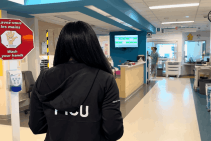 Vue de dos de la Dre Awrad Almesafer, unes des fellows internationaux au Québec, originaire du Koweït, marchant dans le corridor de l'Unité de soins intensifs pédiatriques du Centre universitaire de santé McGill. Elle porte une veste noire sur laquelle est inscrit « PICU ».