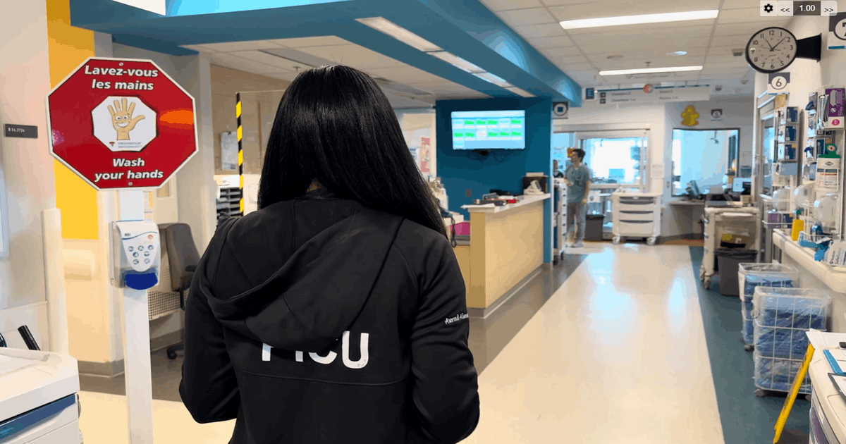 Vue de dos de la Dre Awrad Almesafer, unes des fellows internationaux au Québec, originaire du Koweït, marchant dans le corridor de l'Unité de soins intensifs pédiatriques du Centre universitaire de santé McGill. Elle porte une veste noire sur laquelle est inscrit « PICU ».